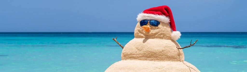 Smiling sandy snowman with red santa hat on the caribbean beach. Holiday concept for New Year and Christmas Cards